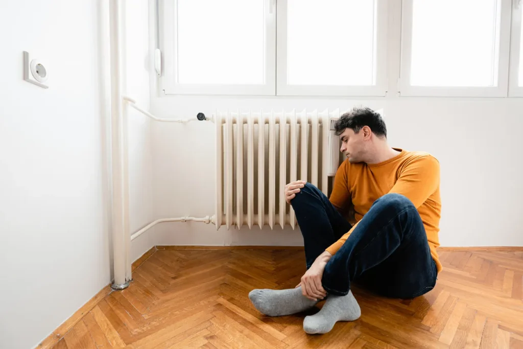 Trustworthy Heater Repair for Quick Heating Solutions 3 Man sitting beside a radiator, appearing concerned, in a well-lit room, reflecting the urgency of heater problems requiring professional attention.