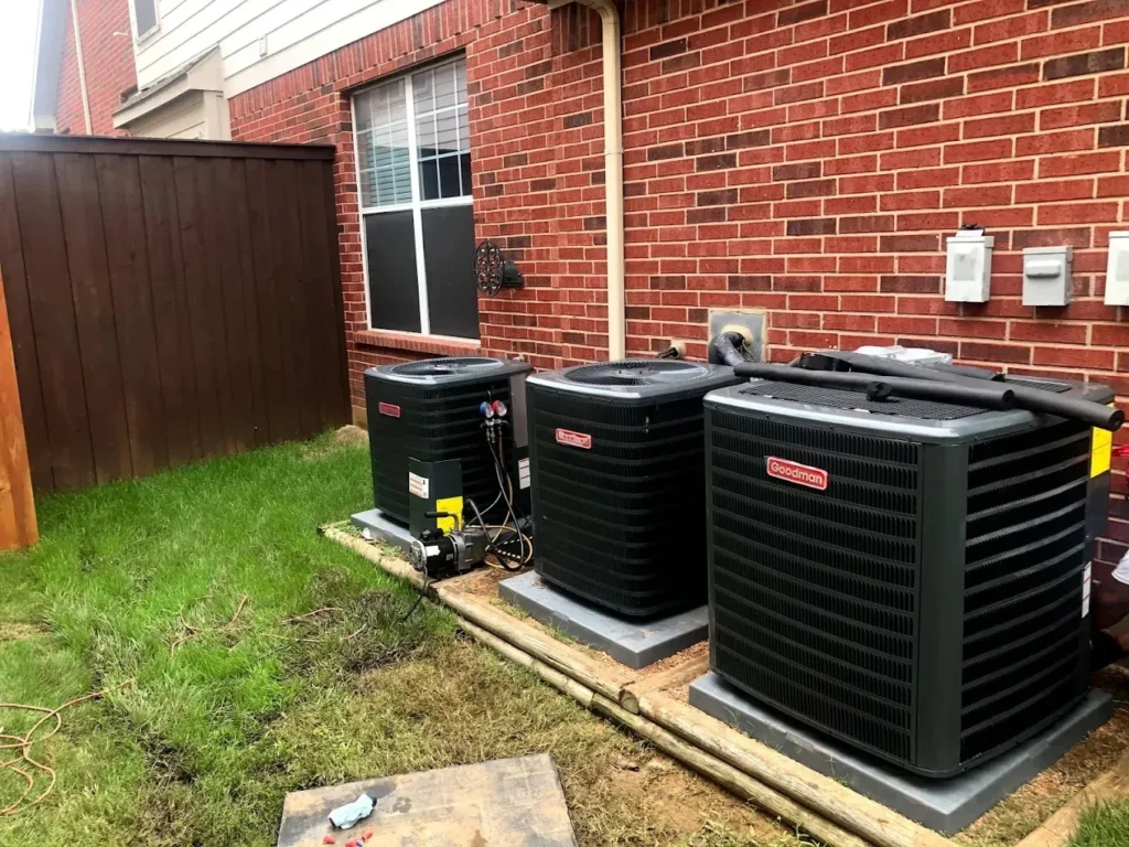 Why Is My AC Not Cooling? Troubleshooting & Repair 2 Three outdoor air conditioning units beside a brick wall and wooden fence.